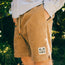A person wearing tan Pressure Drop Cord Shorts made from stretch cotton corduroy with a palm tree patch on the left leg stands outdoors, hands in pockets, enjoying all day comfort. Greenery and sunlight fill the background.