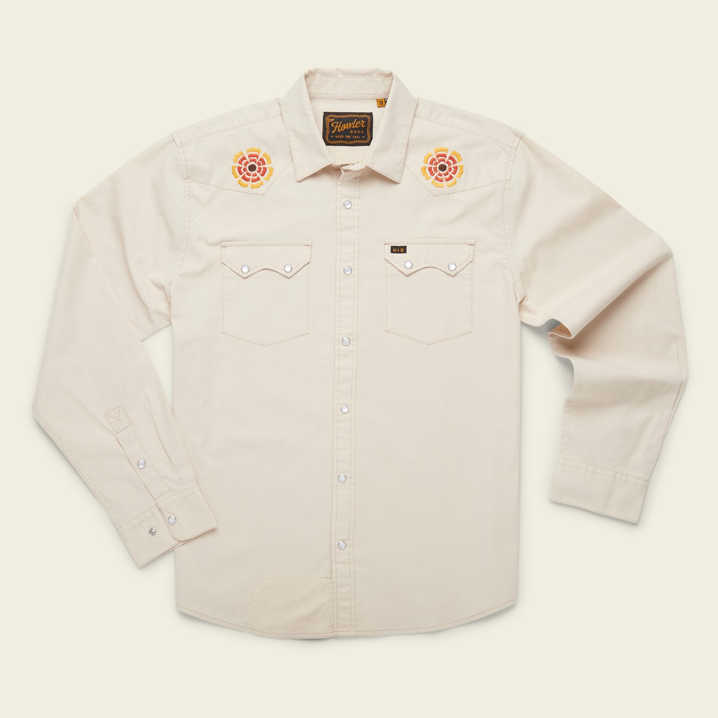 A cream-colored, long-sleeve western shirt crafted from stretch chambray, featuring pearl snaps, two chest pockets, and colorful rose vintage inspired motif embroidery on each shoulder.