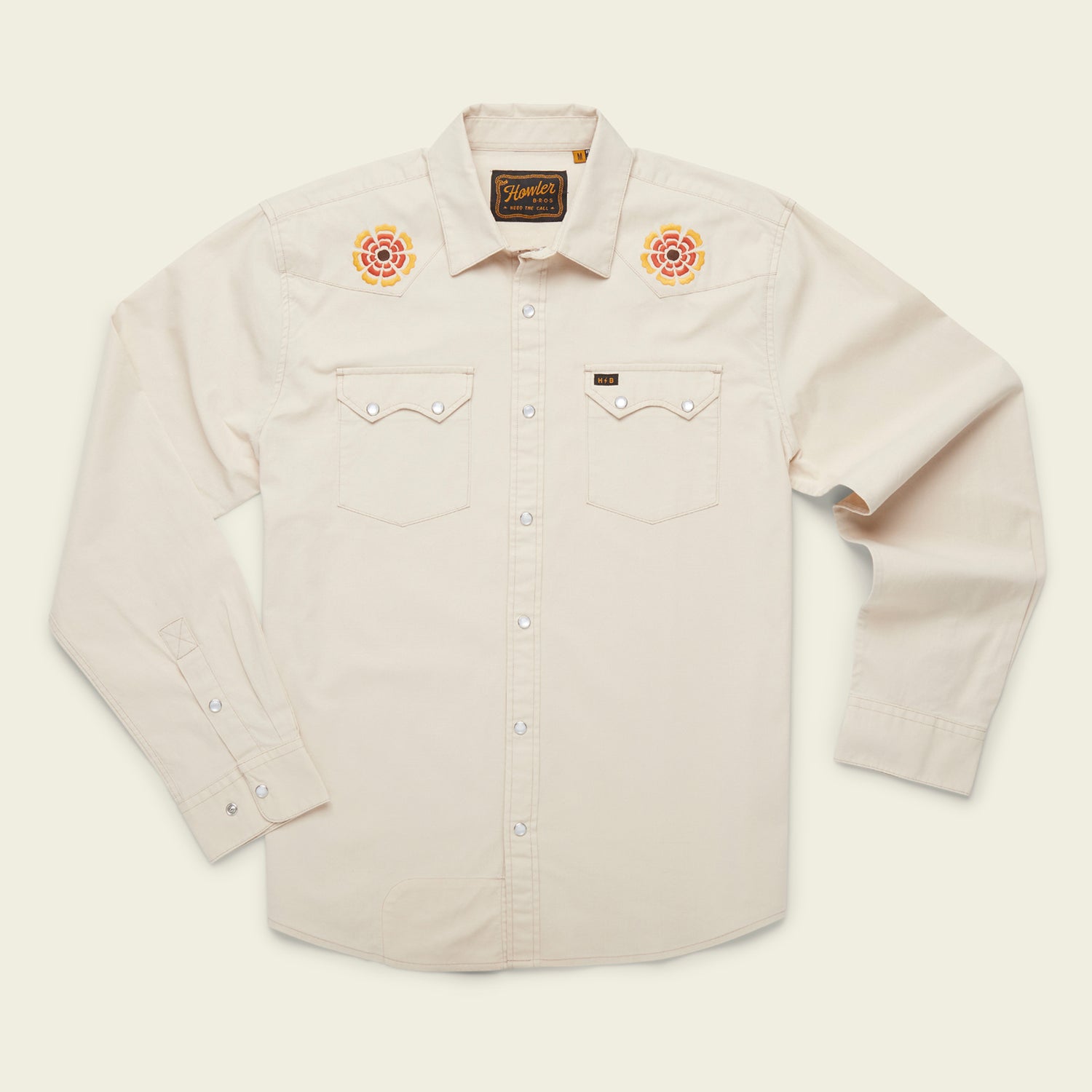 A cream-colored, long-sleeve western shirt crafted from stretch chambray, featuring pearl snaps, two chest pockets, and colorful rose vintage inspired motif embroidery on each shoulder.