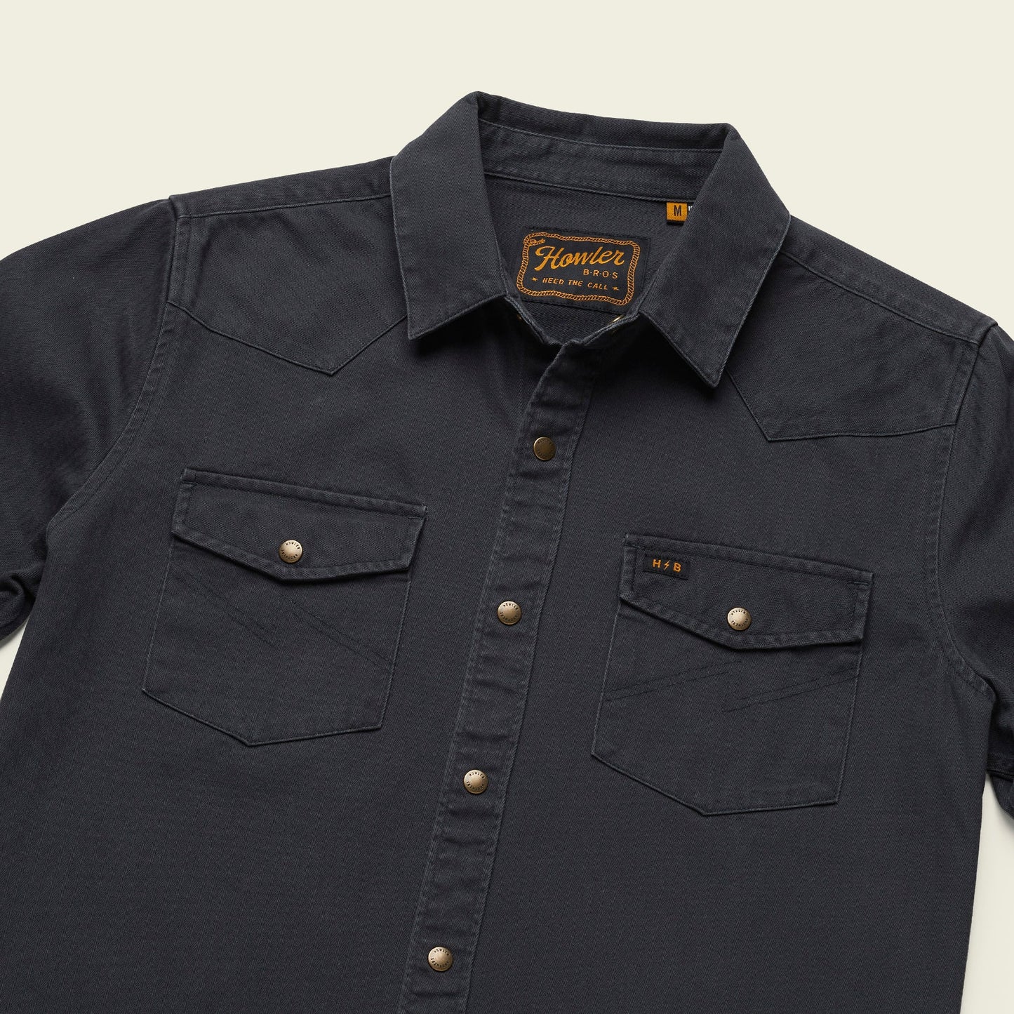 A dark navy Sawhorse Work Shirt with two front chest pockets, each secured by a snap button. The rugged cotton shirt features a pointed collar, gold snap buttons down the front, and a small HOWLER tag on the left pocket.