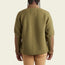 A person wearing a green Howler Crozet fleece jacket with brown elbow patches and tan pants is shown from the back against a plain light background.