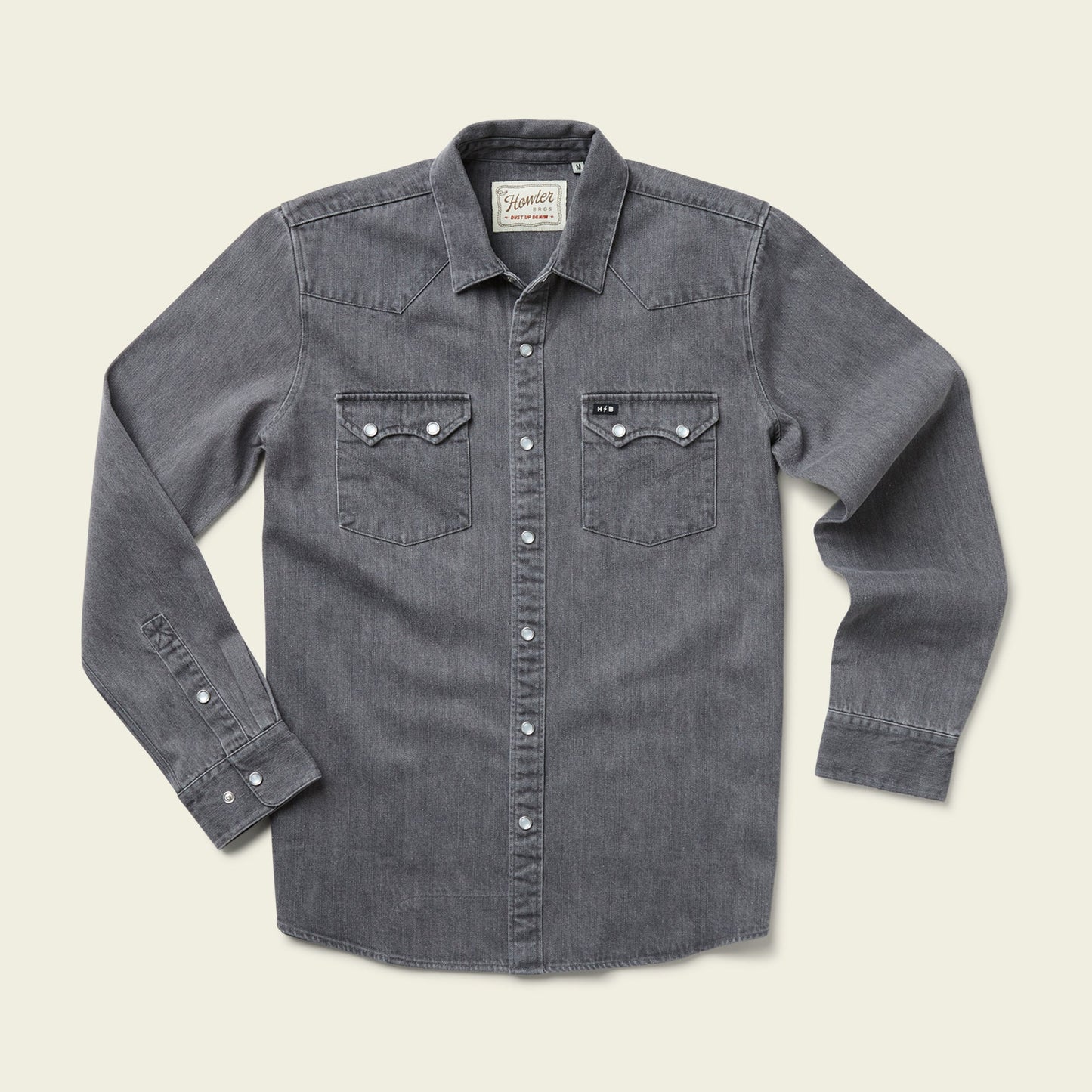 A long-sleeve, button-up gray Denim Snapshirt with two front chest pockets and white buttons, laid flat on a light beige background—perfect for those seeking versatile style.