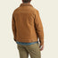 A person wearing the Fuzzy Depot Jacket—a light brown corduroy jacket with a sherpa lining—khaki pants, and a blue plaid shirt stands facing away from the camera against a light background.