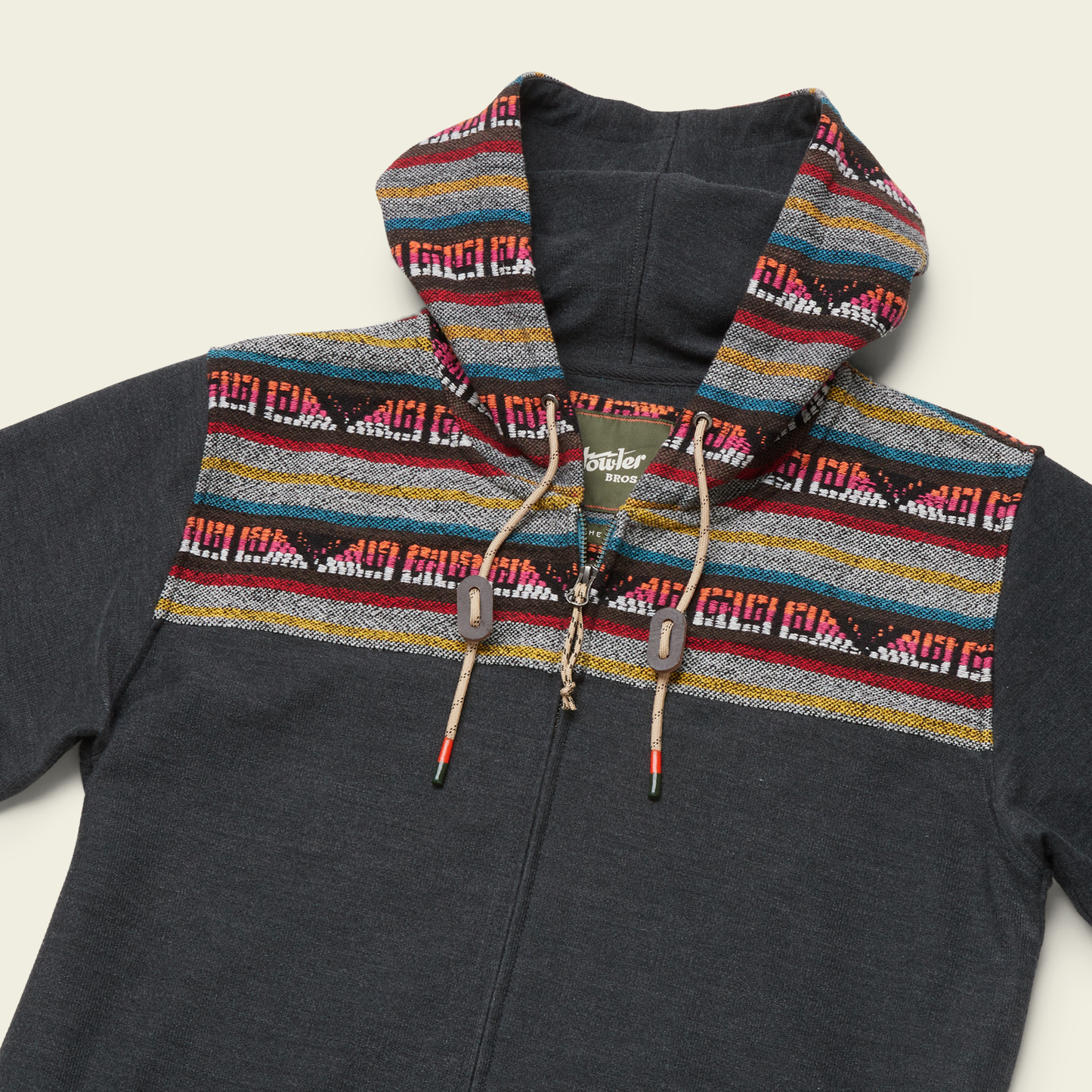 A dark gray cotton blend hoodie with a woven jacquard yoke on the hood and shoulders, showcasing red, yellow, blue, and white designs. Features a zipper front and tan drawstrings with wooden accents.