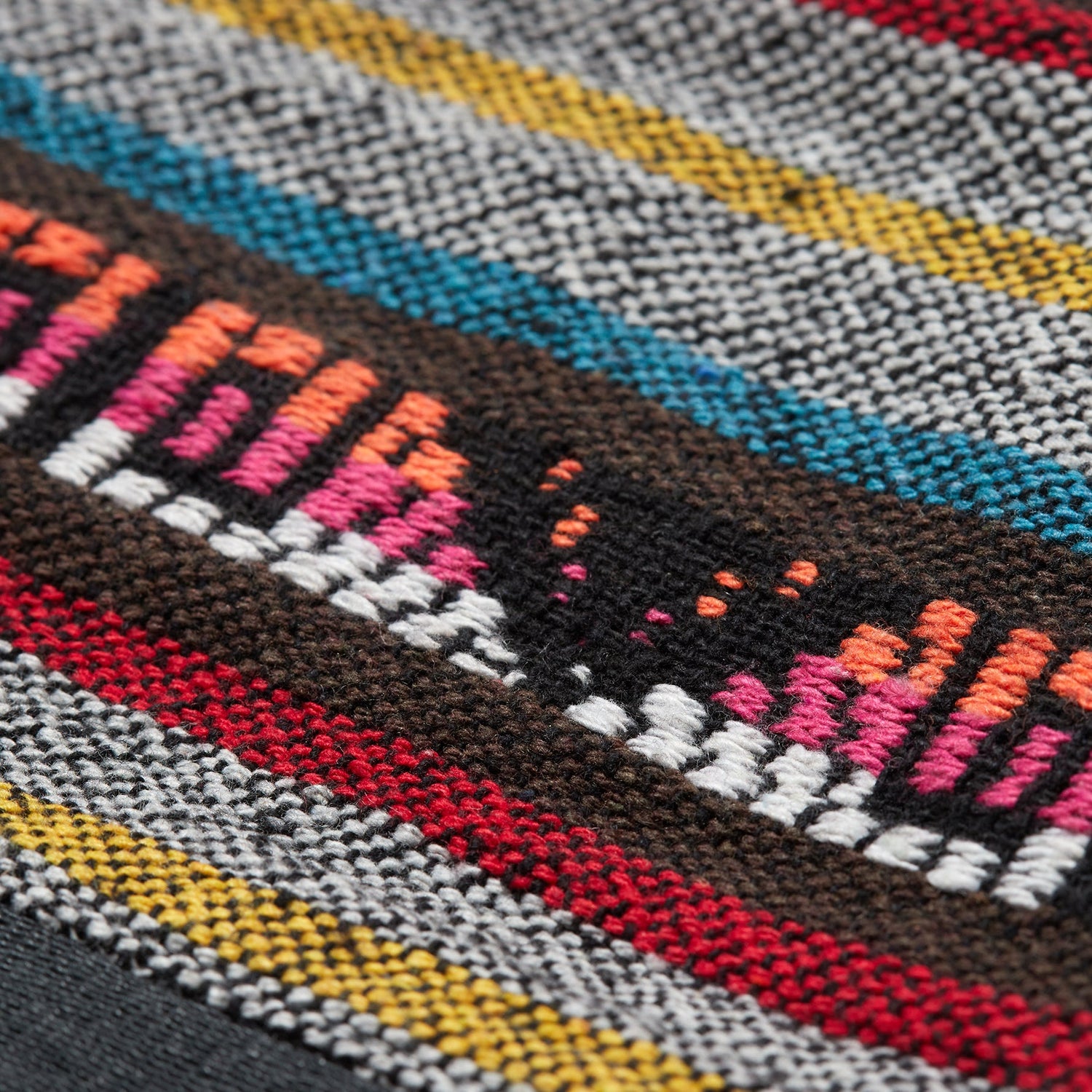 A close-up of a woven jacquard hoodie fabric with colorful horizontal stripes in gray, red, yellow, blue, brown, orange, pink, and white, showing a textured and detailed pattern.