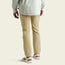 A person wearing light beige tech pants, a light striped long-sleeve shirt, and white sneakers, shown from the back, standing against a plain light background.
