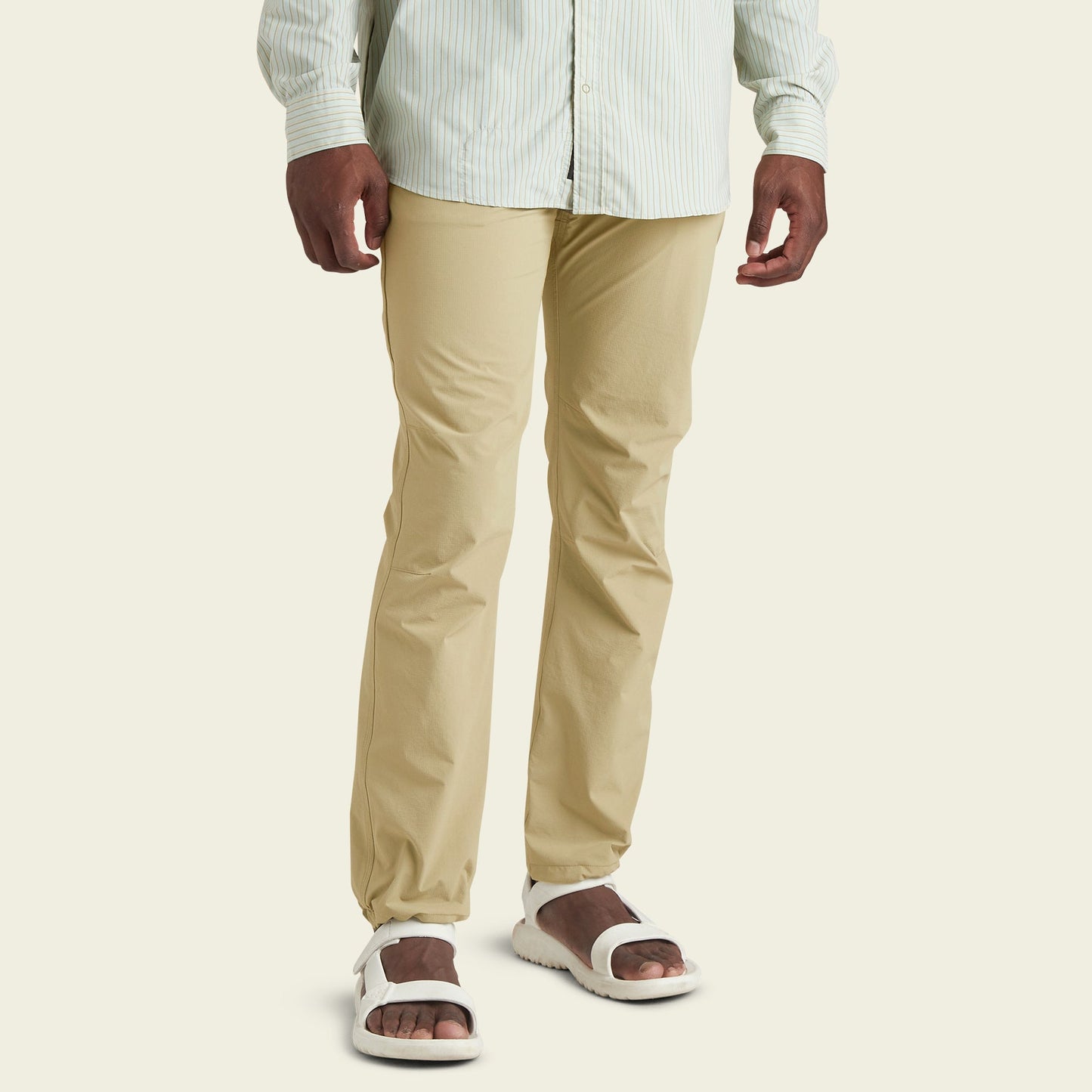 A person wearing light beige stretch nylon pants, a light green and white striped shirt, and white sandals stands against a plain, light background. The image shows the person from mid-chest down.