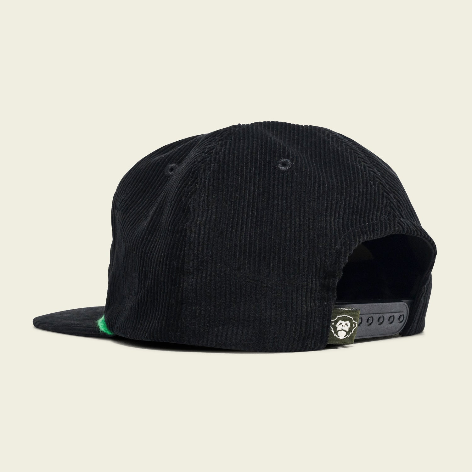 A black corduroy Unstructured Snapback from the 2024 Verde Collection, shown from the back-left side, features an adjustable strap and a small label with a white cartoon gorilla face above the opening.