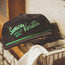 A black corduroy cap from the 2024 Verde Collection with green embroidery reading Somos Verdes HOWLER BROS rests on top of a wire basket filled with towels.