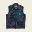 The Chisos Fleece Vest is a lightweight vest featuring high pile fleece, a purple and dark green camouflage pattern, front zipper, two side pockets, and a teal chest pocket with Huckberry label, displayed on a light background.