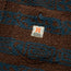 Close-up of a brown and blue high pile fleece fabric with a small rectangular tag. The tag displays an orange H, the word BROS, and the phrase HEED THE CALL.
