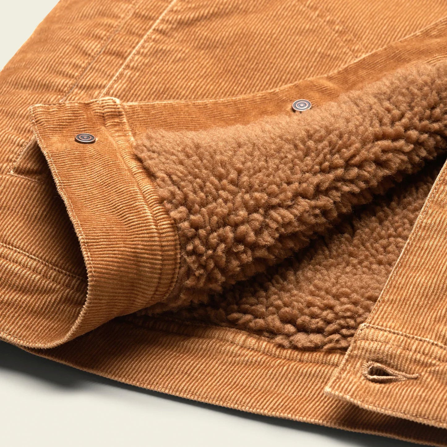 A close-up of the Fuzzy Depot Jacket, a tan corduroy jacket with soft, brown sherpa lining, featuring metal snap buttons and detailed stitching on the fabric.
