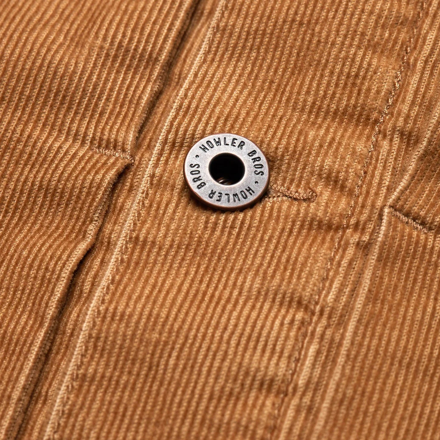 Close-up of a brown corduroy jacket from the Fuzzy Depot Jacket collection, featuring a metal button engraved with HOWLER BROS attached to a seam running vertically through the fabric.