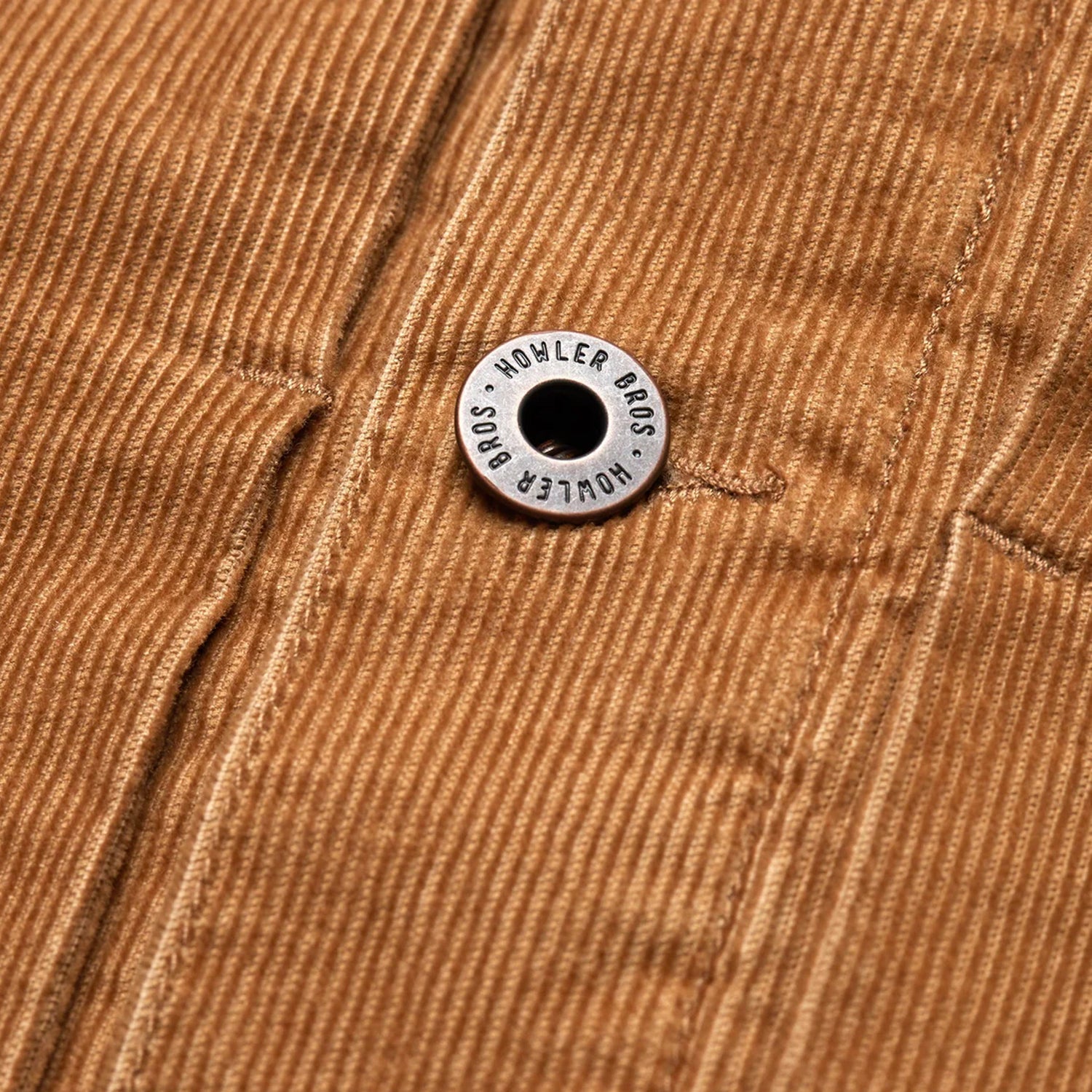 Close-up of a brown corduroy jacket from the Fuzzy Depot Jacket collection, featuring a metal button engraved with HOWLER BROS attached to a seam running vertically through the fabric.
