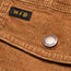 Close-up of brown corduroy jacket fabric with a black and yellow “H//B” label and a metal button engraved with “HOWLER BROS.”—a signature detail on the Fuzzy Depot Jacket.