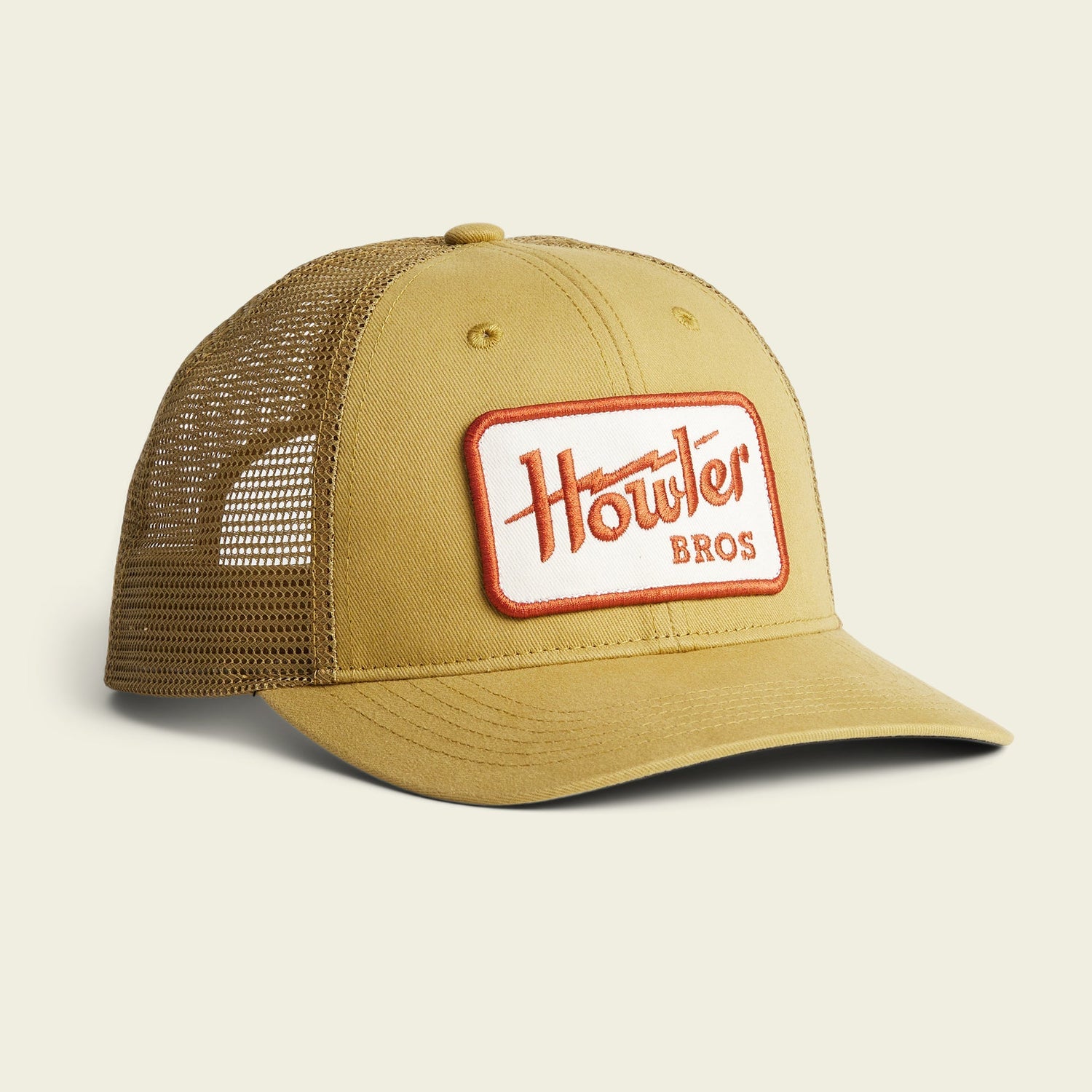 A tan mesh trucker hat with a curved brim and a rectangular patch on the front reading Howler Bros in red and orange letters. This adjustable hat features classic Howler artwork and is displayed on a plain light background.