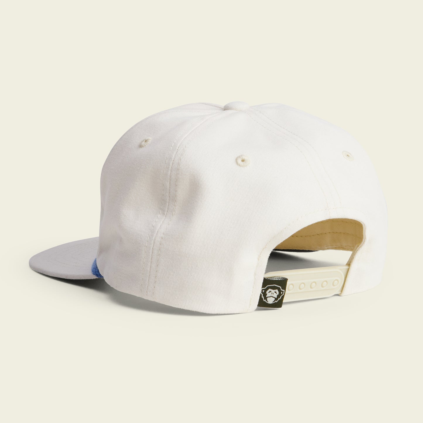 A white baseball cap shown from the back, featuring an adjustable snapback closure and a soft crown for comfort. A small black tag with a monkey face logo sits near the closure, while the brim is light gray. Ideal for fans of Unstructured Snapbacks.