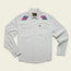 A light gray, long-sleeve stretch chambray button-up shirt with pearl snaps, two chest pockets, and colorful, vintage inspired motif embroidery in pink, purple, and blue on each shoulder. The shirt is laid flat on a cream background.