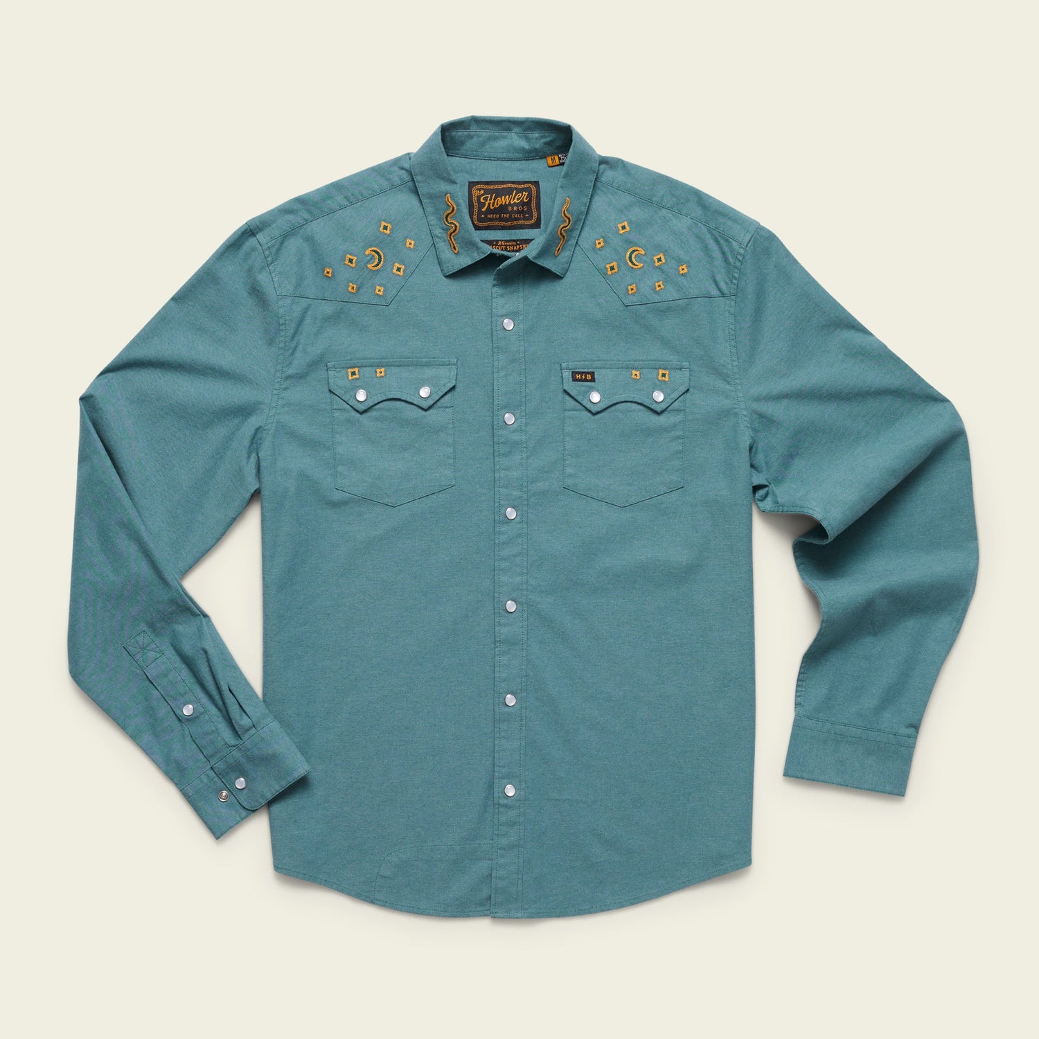 A teal long-sleeve western shirt in stretch chambray, featuring pearl snaps, two chest pockets, and gold vintage inspired motif embroidery of stars and cacti on the yoke. The shirt is laid flat on a light background.
