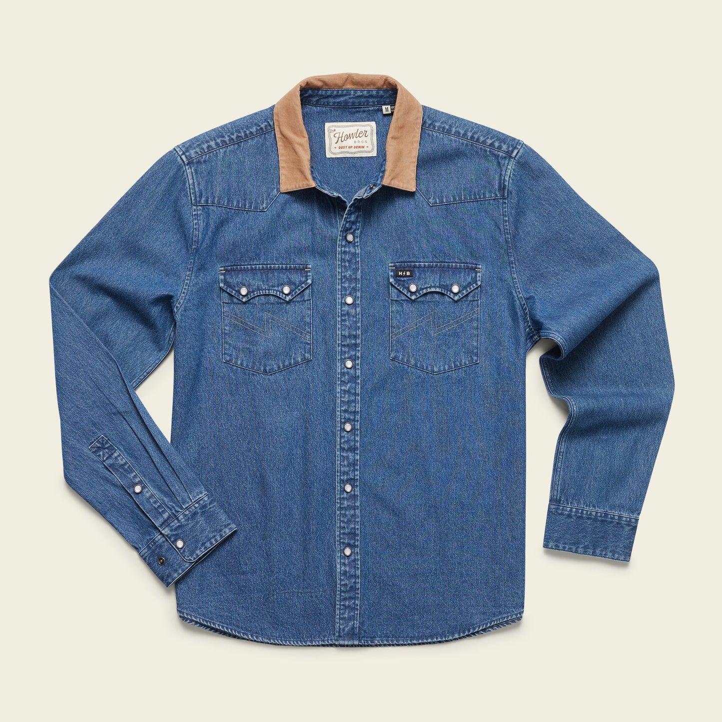 A rugged cotton shirt, this blue denim long-sleeve features a tan corduroy collar, pearl snap buttons, and two front chest pockets, blending versatile style with classic Denim Snapshirts flair. Laid flat on a light background.
