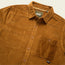 A brown wide wale corduroy button-up shirt with a collar and single chest pocket, featuring brown buttons and a visible Howler Bros label inside the neckline—perfect as an Iquitos Overshirt or travel shirt.