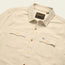 A beige western shirt with a collar, two front chest pockets with button flaps, and brown buttons. The Novato Shirt features a visible Howler Bros brand tag inside the collar and above the left pocket.