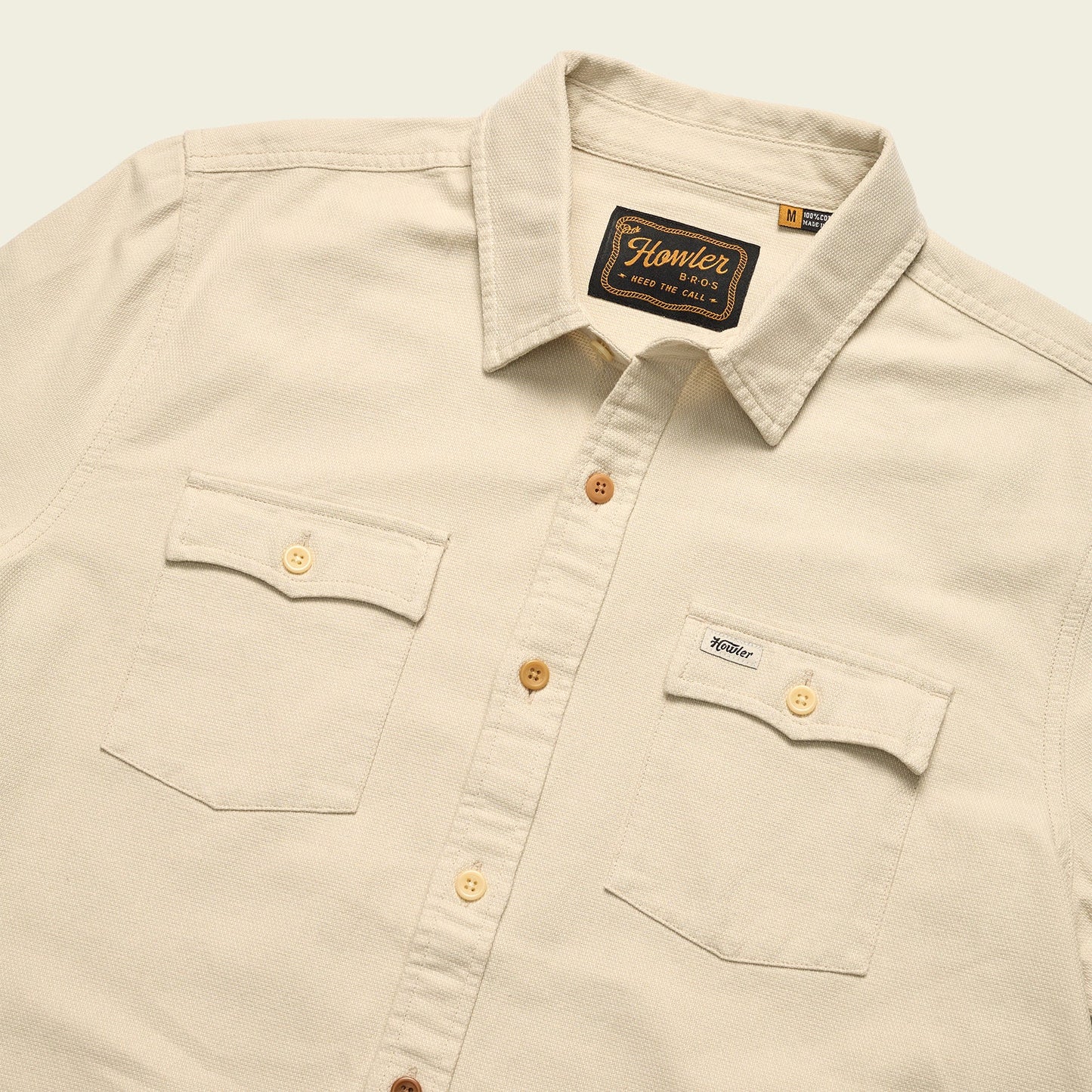 A beige western shirt with a collar, two front chest pockets with button flaps, and brown buttons. The Novato Shirt features a visible Howler Bros brand tag inside the collar and above the left pocket.