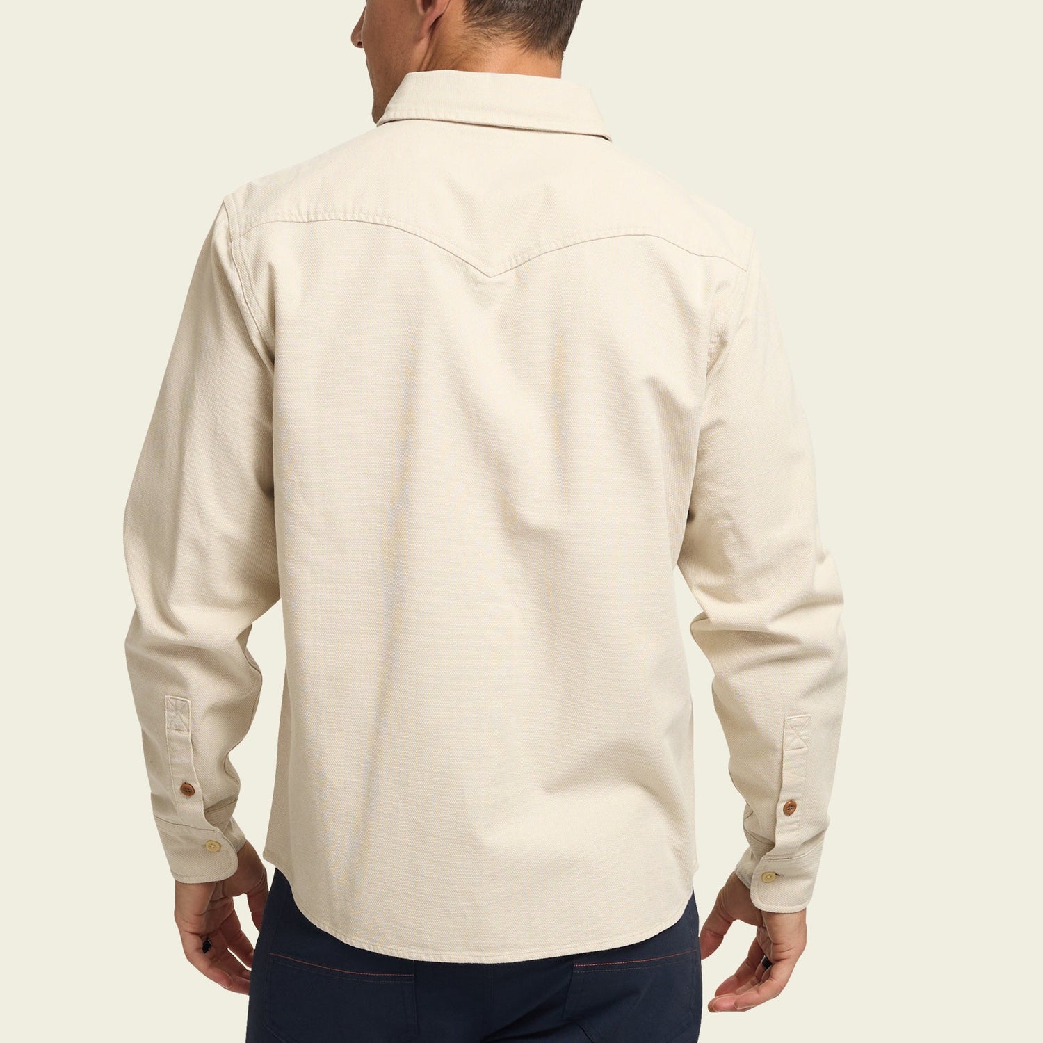 A man wearing a cream-colored, long-sleeve Novato Shirt with a yoke detail on the back, shown from behind against a plain light background.