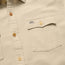 Close-up of a beige Novato Shirt, a classic western shirt with light brown buttons and a chest pocket. The pocket flap features a small Howler label and is secured by a button.