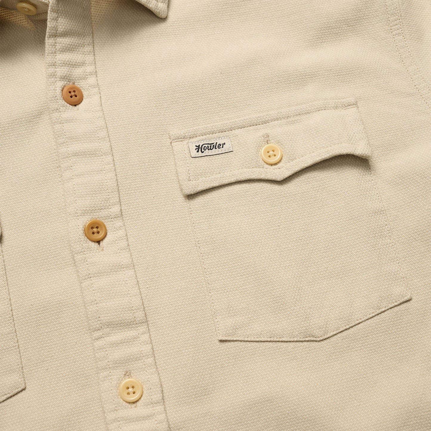 Close-up of a beige Novato Shirt, a classic western shirt with light brown buttons and a chest pocket. The pocket flap features a small Howler label and is secured by a button.