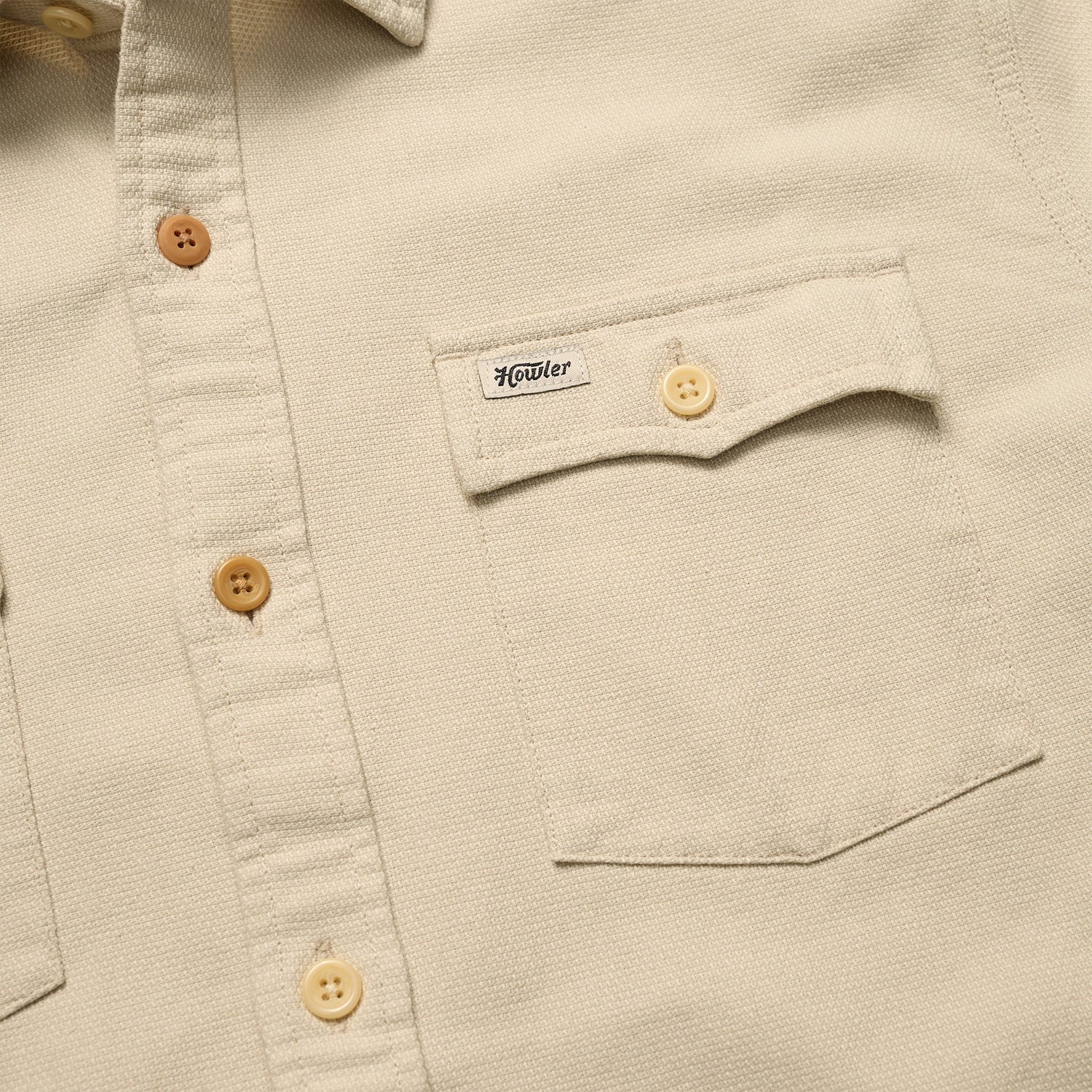 Close-up of a beige Novato Shirt, a classic western shirt with light brown buttons and a chest pocket. The pocket flap features a small Howler label and is secured by a button.