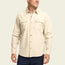 A man wearing a long-sleeve, cream-colored Novato Shirt with two chest pockets and dark pants stands against a plain light background.