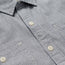 Close-up view of a light gray Tallier Work Shirt, crafted from cotton chambray, with white buttons and visible stitching details around the buttonholes and pockets—an elevated nod to classic American workwear.
