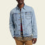 A person wearing a light blue Depot Jacket with lightning bolt stitch over a red and blue plaid shirt and a patterned shirt, paired with tan pants, stands against a plain light background.