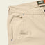 Close-up of the front pocket and waistband of light beige utility pants with visible stitching, silver rivets, and a green and orange “Howler Bros” label on the inside waistband.