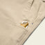 A close-up of rugged backcountry pants with a pocket knife featuring a brass handle partially visible in the front pocket.