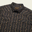A black western shirt with tan floral and stripe patterns, featuring two front chest pockets with flaps and pearl snaps, plus a woven Howler Bros label on the inside collar.