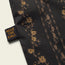 A close-up of a black western shirt fabric with a brown floral pattern and a sewn black tag that reads HEED THE CALL in orange letters, highlighting the distinct style of the H Bar B Snapshirt.