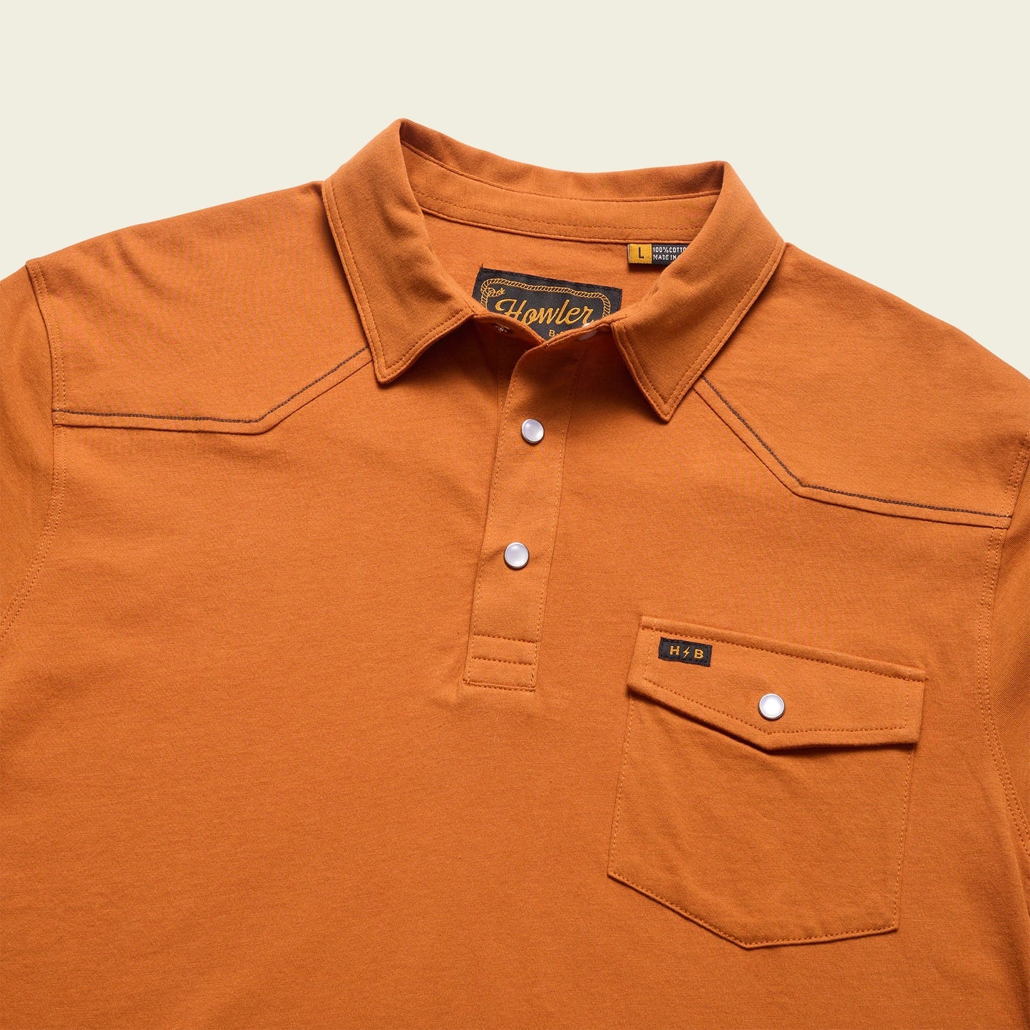 An orange Ranchero Polo crafted from heathered cotton, featuring a button-up placket, front chest pocket, subtle stitching details, and white buttons. The visible Howler brand label inside the collar adds to its western style polo charm.