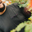 A person wearing a Howler Brothers pocket t-shirt with a patterned pocket stands among green foliage and orange flowers, smiling. Only the lower half of their face and upper torso are visible.