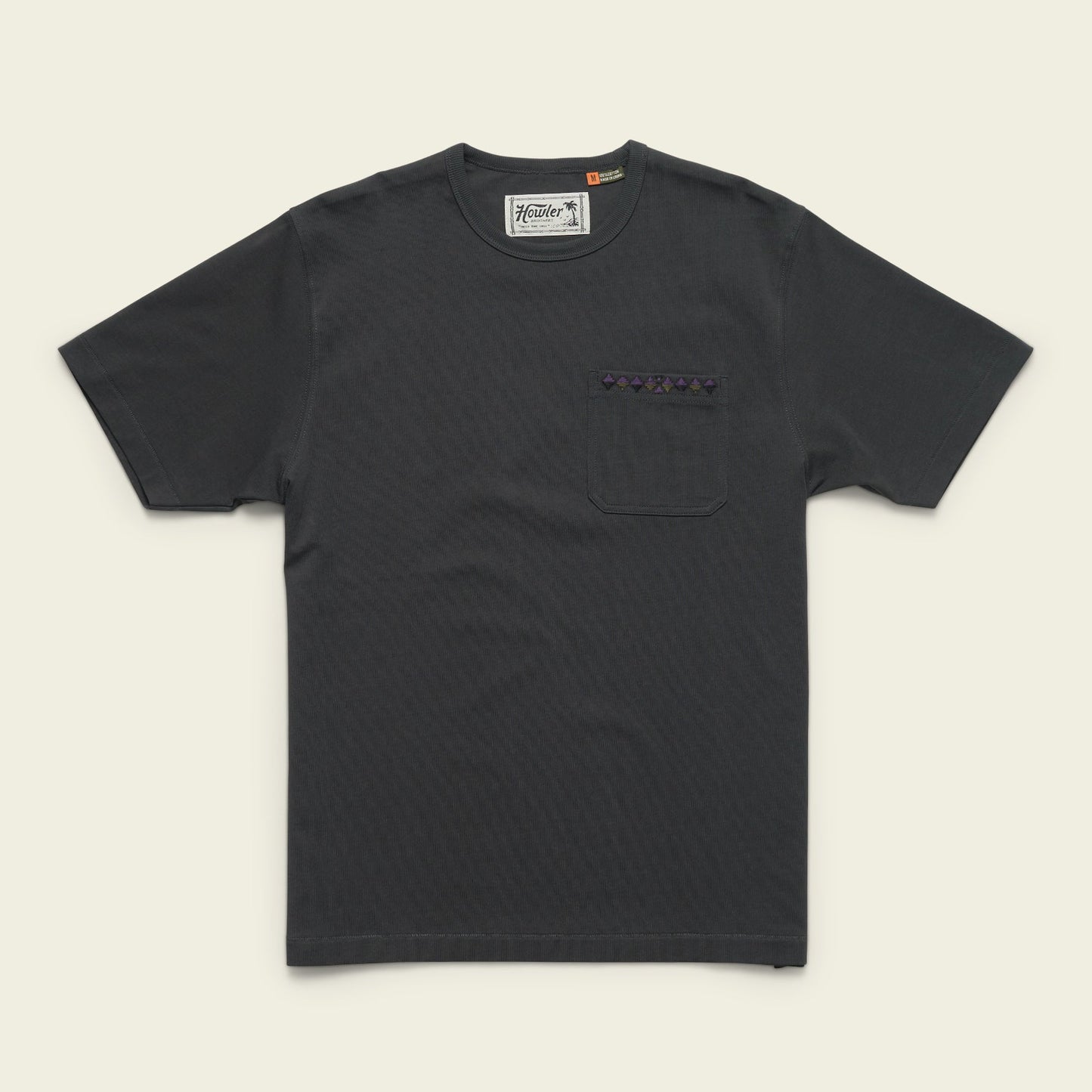 A plain black heavyweight cotton pocket t-shirt with a chest pocket featuring a small patterned strip above it, laid flat on a light background.