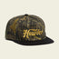 A camouflage-patterned baseball cap with a black brim and the word Howler embroidered in yellow on the front, featuring an adjustable snapback closure and a soft crown for all-day comfort.