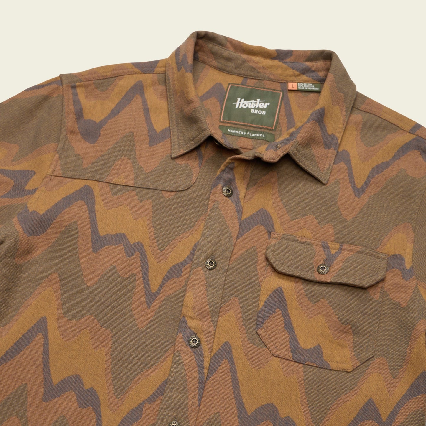 A brown and tan long-sleeve button-up Harkers Flannel shirt with an abstract zigzag pattern, featuring a single chest pocket, collar, and reinforced elbow patches. The tag inside reads Howler Bros.