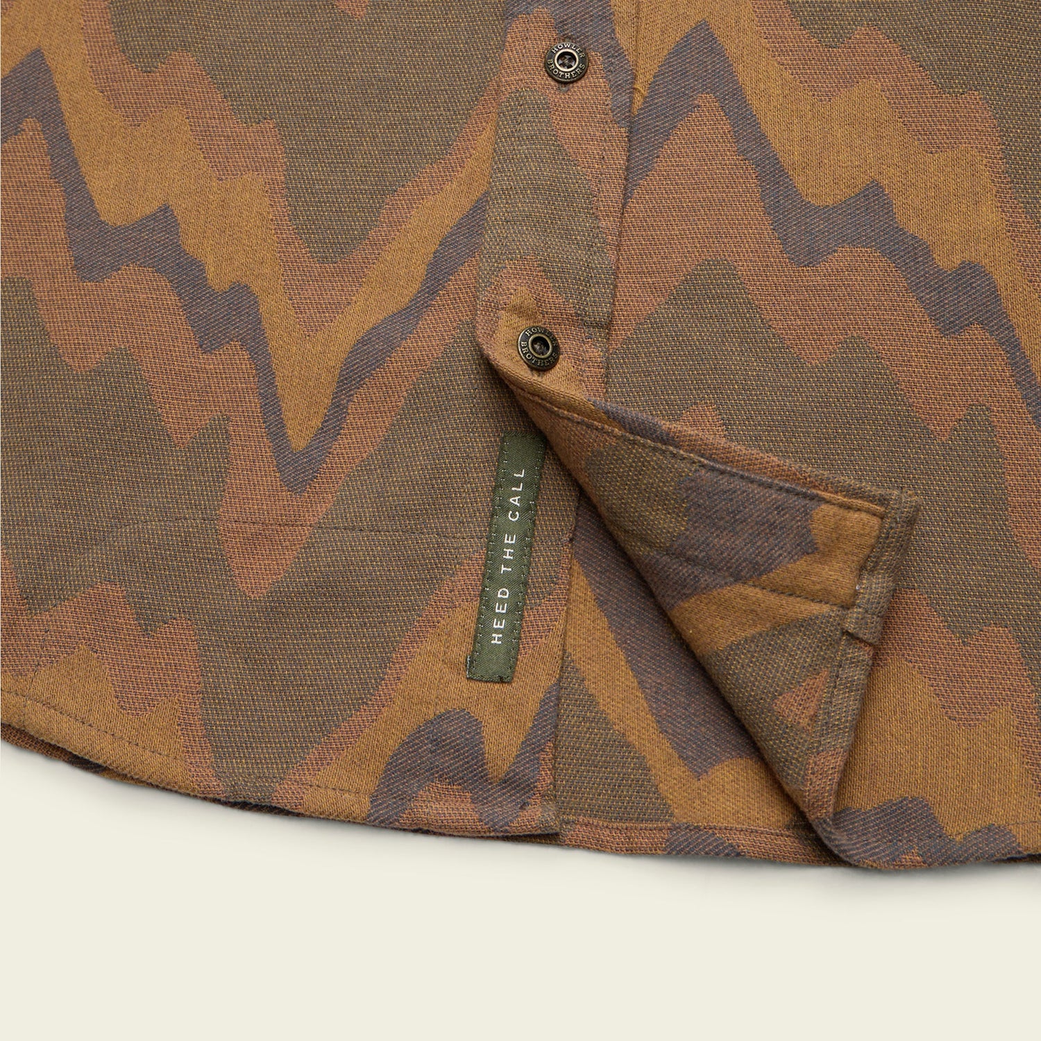 Close-up of a shirt with a brown and tan wavy, abstract pattern in buttery soft flannel. A small green tag reading HEED THE CALL is sewn on the inside hem and unbuttoned placket.