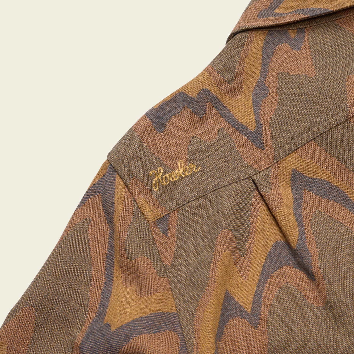 A close-up of a brown and tan patterned buttery soft flannel fabric with the word Howler embroidered in yellow on the shoulder area of a garment, possibly a jacket or shirt.