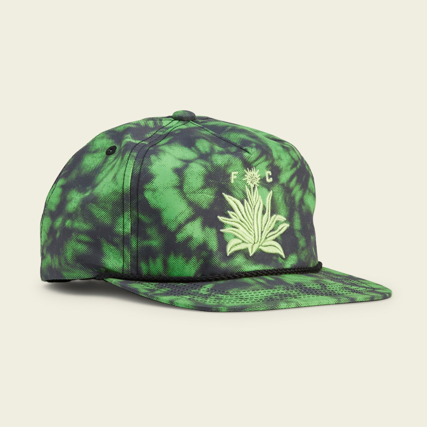 A green and black tie-dye baseball cap inspired by Austin FC, featuring an embroidered plant design and the letters F C on the front. This stylish Howler Brothers snapback has a flat brim and a decorative black rope across the crown’s base.