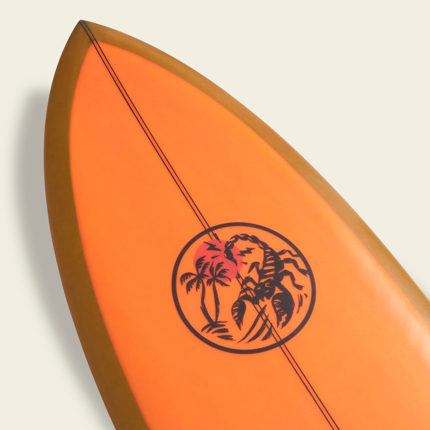 Close-up of the tip of an orange Almond Surfboards surfboard with a circular black graphic featuring palm trees and a setting sun, on a plain light background.