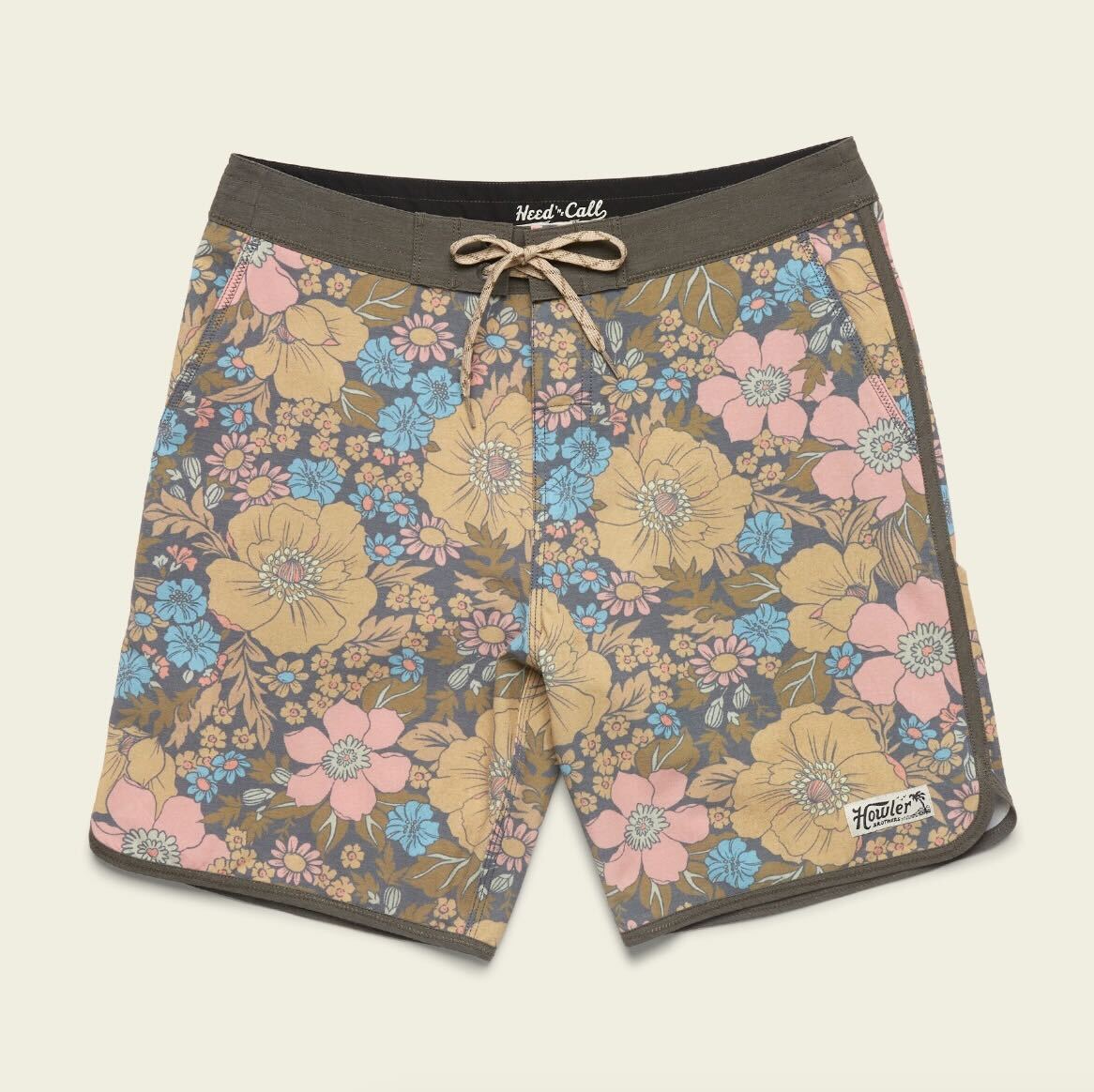 A pair of Bruja Boardshorts with a drawstring waist, made from stretchy fabric and featuring a colorful floral pattern in yellow, blue, and pink on brown, plus Howler branding on the left leg.
