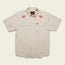 A Crosscut Deluxe Shortsleeve summer shirt in light beige, featuring two front pockets and striking red-orange sunburst motif embroidery on each chest, displayed flat on a pale background.