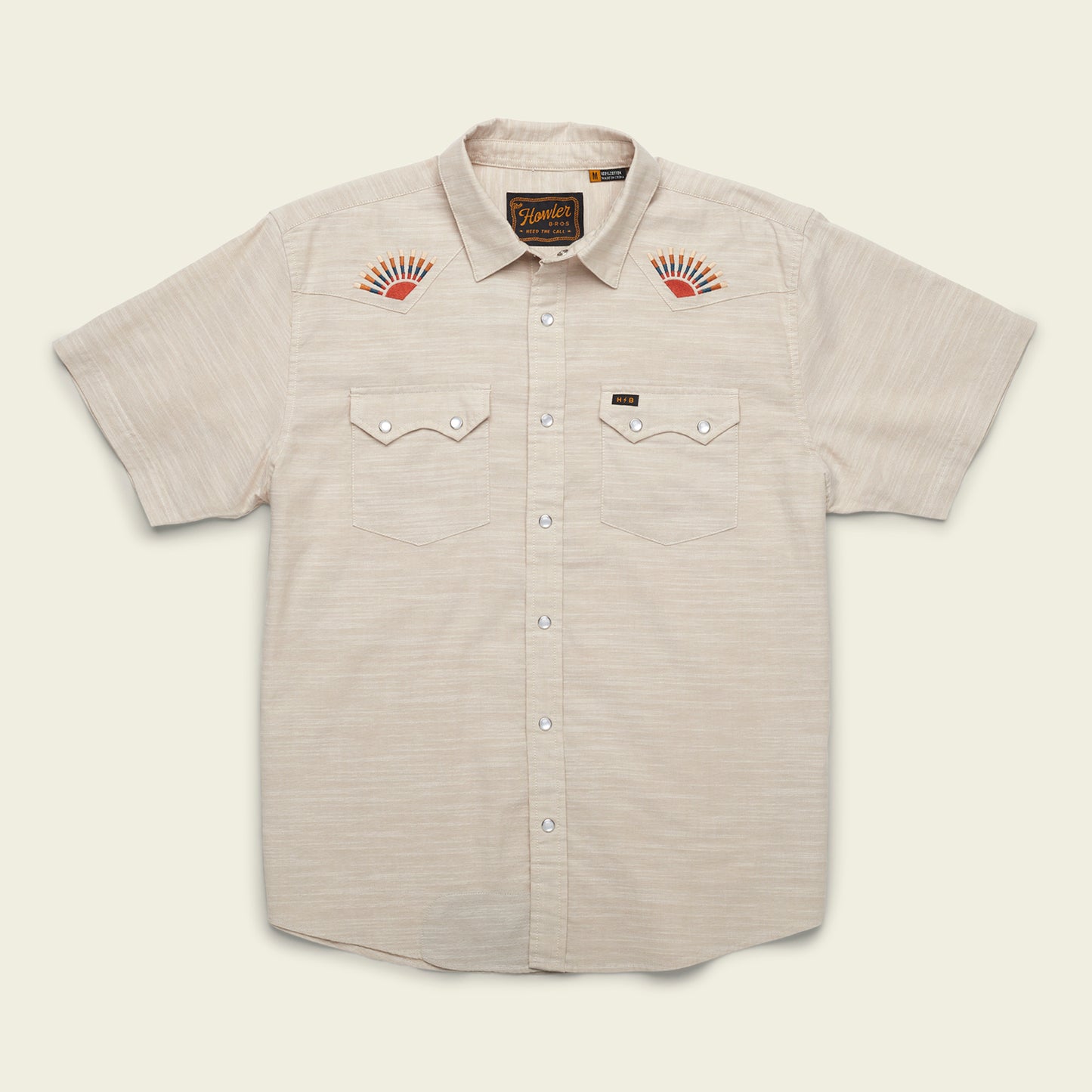 A Crosscut Deluxe Shortsleeve summer shirt in light beige, featuring two front pockets and striking red-orange sunburst motif embroidery on each chest, displayed flat on a pale background.